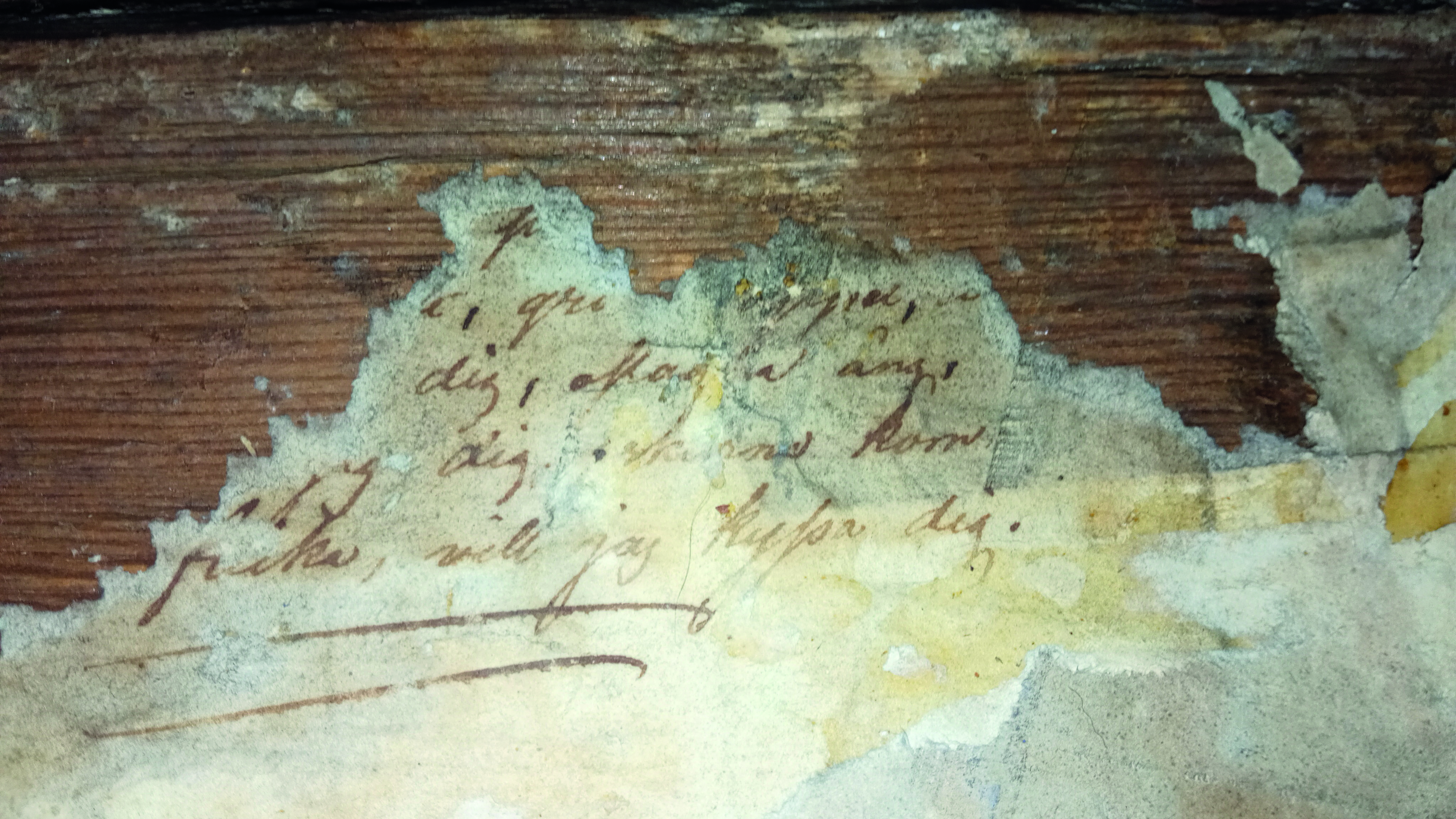 Färgfotografi av det slitna manuskriptet tapetserat på väggen. Upptill syns väggstocken.